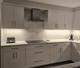 Left wall of a custom U-shaped kitchen, Hillsboro Beach, Florida, featuring OneSkin Sunny White Super Matte flush-panel cabinetry, Tuscani Quartz countertops and backsplash, stainless steel cooktop with range hood, and custom flush-mounted recessed LED under-cabinet lighting with concealed wiring.